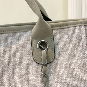 Detalle del asa de cuero verde claro y textura de lona beige con cadena de plata