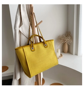 Detalle de bolso tote de lona amarilla con tejido texturizado y asas de cadena y piel