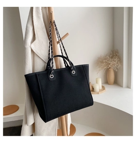 Detalle de bolso tote de lona negra con correa de cadena colgado en perchero de madera
