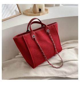Detalle de bolso tote de tweed rojo con asas de cuero y correa de hombro de cadena trenzada