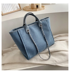 Detalle del bolso tote de lona azul con asas de cuero y cadena decorativa plateada