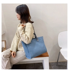 Vista detallada del bolso tote denim azul claro con correa de cadena en modelo femenina