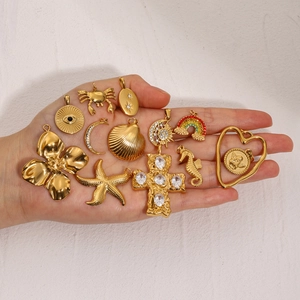 Detailed collection of 18k gold stainless steel charms like starfish and crosses on hand
