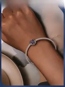 Detail of silver mesh bracelet with purple heart charm and feather design on wrist