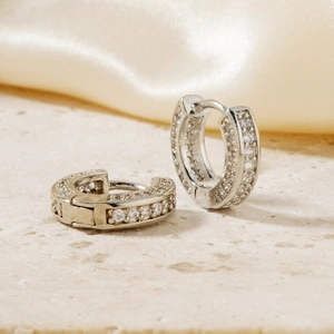 Silver huggie hoop earrings with micro-pave zirconia stones on marble background
