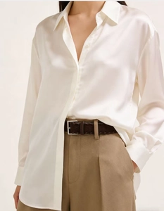 Detail of a brown woven belt styled with a white silk shirt and khaki trousers