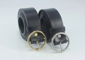 Detail of black leather belts showing silver and gold round buckles in a studio setting