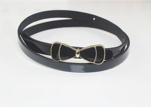 Detail of black patent leather skinny belt featuring a gold-edged bow buckle and adjustment holes