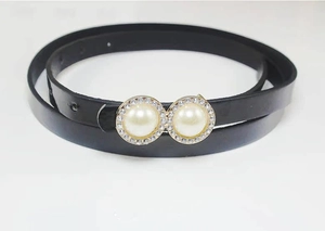 Close-up of black patent leather belt featuring twin pearl buckle with rhinestone trim