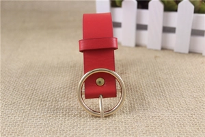 Close-up of red leather belt with a polished gold round buckle on beige fabric