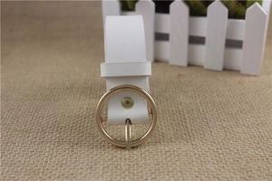 Close-up of white faux leather belt with a round golden buckle and metallic rivet detail