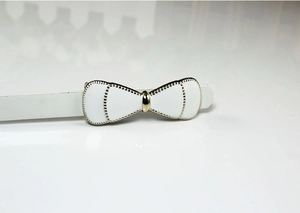 Detail view of a white enamel bow belt buckle with golden beaded edges on a glossy surface