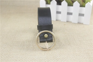 Close-up of black PU leather belt with a round gold buckle on beige textured fabric