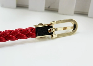 Detail of red braided leather belt with a polished gold horseshoe buckle and pin closure