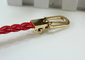 Detail of red woven thin belt featuring a brushed gold metal buckle on white background