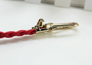 Macro detail of red braided leather belt with polished golden metal lobster clasp