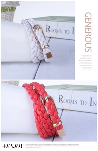 Detail of red and white woven belts with gold buckles on books and ceramic vase