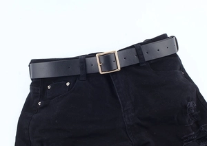Close-up of black leather belt with square gold buckle on black ripped jeans