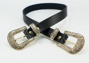 Detailed close-up of vintage Western belt featuring double gold engraved buckles on black leather