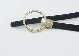 Détail d'une fine ceinture en cuir noir avec boucle ronde dorée et fixations à vis