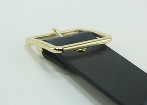 Close-up of black leather belt featuring a polished gold rectangular metal buckle