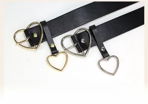 Detail of heart-shaped buckle and pendant on black leather belts in gold and silver finish