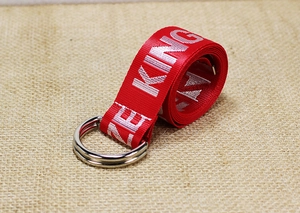 Detail of red nylon belt featuring white embroidered letters and silver double D-ring buckle