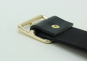 Detailed view of black leather belt with a polished gold square buckle and rivet detail