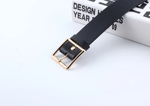 Detail of minimalist black leather belt featuring a polished gold square metal buckle