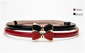 Détail de ceintures fines en cuir verni rouge et noir avec boucles nœud dorées