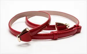 Détail d'une fine ceinture en cuir verni rouge avec une boucle en métal doré poli