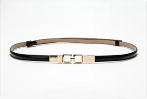 Detailed close-up of a slim black patent leather belt featuring a gold geometric buckle