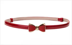 Détail d'une ceinture fine en cuir verni rouge avec boucle dorée en forme de nœud