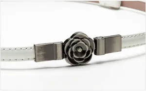 Close-up of a white patent leather skinny belt featuring a camellia flower metal buckle