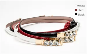 Three skinny faux leather belts in white, red and black with gold rhinestone buckles