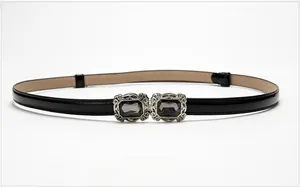 Detail of skinny black patent leather belt featuring grey gemstone double buckle design