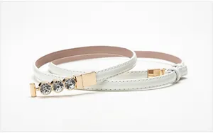 Close-up of a slim white faux leather belt featuring a gold buckle with three large rhinestones