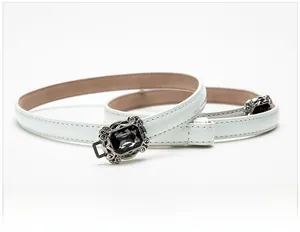 Close-up of a white patent leather thin belt featuring a vintage hollow metal buckle with gemstone