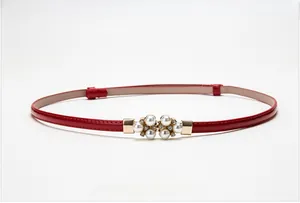 Dettaglio di cintura sottile in vernice rossa con fibbia elegante in perle