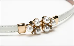 Dettaglio di una cintura bianca in pelle con fibbia dorata decorata con perle e strass lucidi