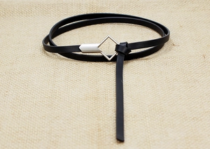 Detail of a thin black leather belt with a silver geometric buckle on a beige linen surface