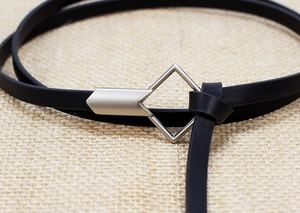 Close-up of slim black leather belt with silver diamond buckle on linen background