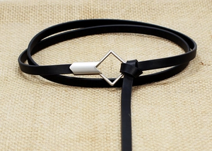 Detail of slim black leather belt with silver geometric buckle on beige linen background