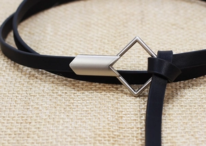 Close-up of a slim black leather belt featuring a matte silver geometric buckle on burlap