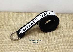 Détail d'une ceinture en toile noire avec lettrage MASKED BALL blanc et boucle en D argentée