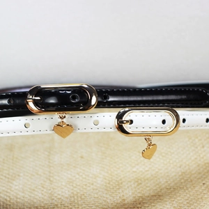 Slim patent leather belts for women in black and white with golden oval buckle and heart pendant