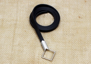 Close-up of a slim black leather belt with silver square buckle on a burlap background