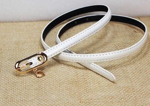 Detailed view of a white patent leather skinny belt with a gold heart pendant and oval buckle