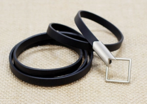Detail of minimalist black silicone belt with matte silver geometric buckle on woven texture
