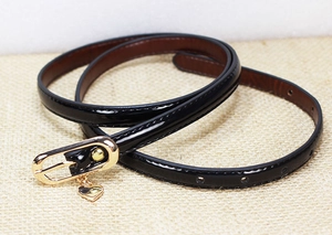 Detail of black patent leather skinny belt with a gold oval buckle and heart pendant